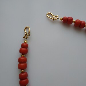 May include: A coral bead necklace with gold clasps. The necklace is made of small, round coral beads and has a simple design.