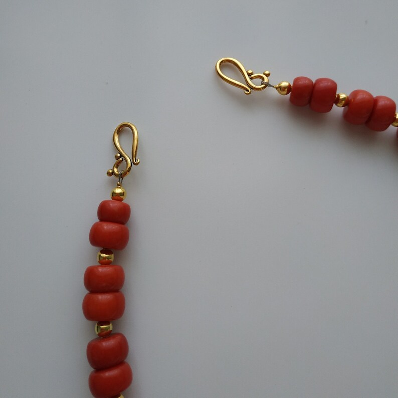 May include: A coral bead necklace with gold clasps. The necklace is made of small, round coral beads and has a simple design.