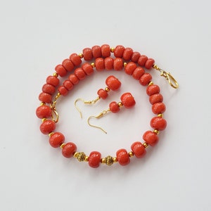 May include: A red coral necklace with gold accents and matching earrings. The necklace is made of round beads and the earrings are drop style.