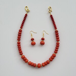 Op de afbeelding: Een rode koraal kralen ketting en oorbellen set. De ketting heeft een gouden sluiting en de oorbellen hebben gouden haken.