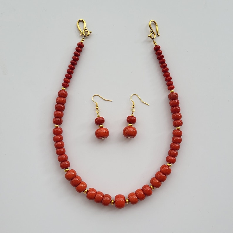 Op de afbeelding: Een rode koraal kralen ketting en oorbellen set. De ketting heeft een gouden sluiting en de oorbellen hebben gouden haken.