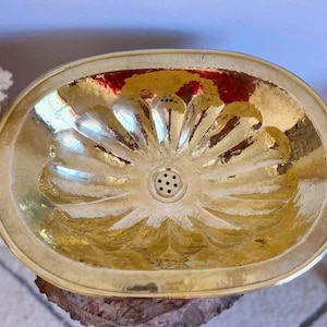 May include: A gold oval-shaped bathroom sink with a decorative, flower-like design. The sink has a drain in the center.