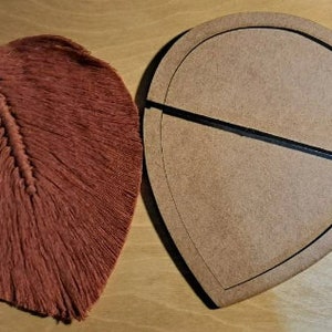 May include: A brown wooden feather-shaped template with a black line down the center. The template is used for crafting and creating a feather-shaped object.