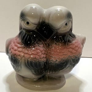 May include: A ceramic figurine of two birds facing each other. The birds have gray heads, pink chests, and black wings. The figurine is on a round base and has a glossy finish.