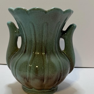 May include: A small, green ceramic vase with two handles. The vase has a scalloped rim and a textured surface.
