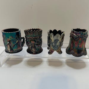May include: Four iridescent glass decorative pieces. The pieces include a small mug with a handle, a face, a paisley design, and a bell shape. The pieces are in shades of blue, green, and purple.