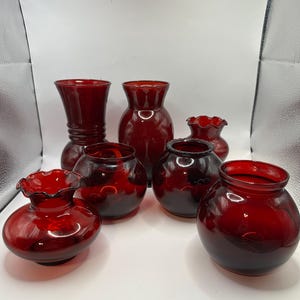 May include: Set of six red glass vases of varying sizes and shapes. The vases have a vintage look and are perfect for displaying flowers or other decorative items.
