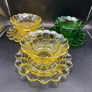 May include: Three glass bowls with scalloped edges. Two are yellow and one is green. The bowls are on matching plates.