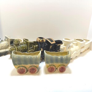 May include: A set of six ceramic train planter pots. The train is made up of five cars, including a green engine, a black engine, a white engine, and two green boxcars. The boxcars are shaped like train cars with wheels.