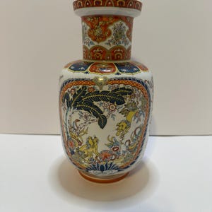 May include: A decorative ceramic vase with a wide base and a narrow neck. The vase features intricate patterns in red, blue, yellow, and white. The design includes floral and animal motifs, creating a detailed and ornate appearance.
