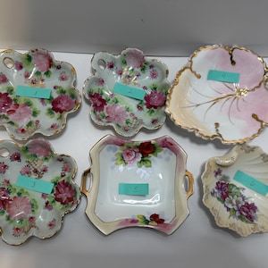May include: A collection of six antique porcelain dishes with floral designs. The dishes vary in shape, including a leaf, a shell, and flower-shaped designs. Each dish features a gold trim and a different floral pattern.