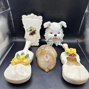 May include: Five ceramic wall decor pieces, including a white framed piece with a butterfly design, a white dog head, a brown acorn, and two white violins with yellow flower accents.