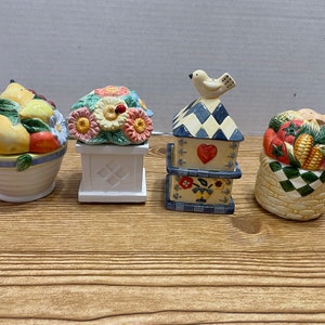 May include: Four ceramic salt and pepper shakers with a farmhouse theme. The shakers are decorated with fruit, flowers, a birdhouse, and vegetables.