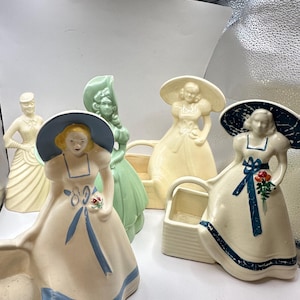 May include: Five vintage ceramic planter figurines of women wearing hats and dresses. The planters are in various colors, including white, green, and blue. Each planter has a small basket-shaped opening for planting.
