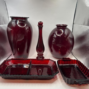 May include: A set of five ruby red glass pieces, including two vases, a bottle, and two serving dishes. The pieces are all made of a deep red glass with a textured surface.