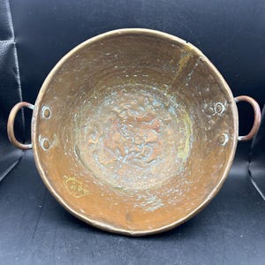 May include: A vintage copper pot with two handles. The pot has a hammered finish and shows signs of age and use.