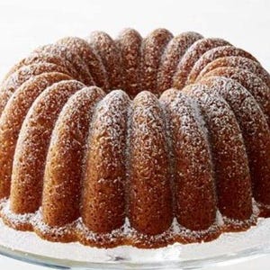 May include: A golden brown bundt cake with a powdered sugar dusting. The cake has a ring shape with a center hole and a textured surface.