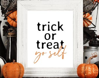 May include: A Halloween-themed display featuring a white framed print with the text "trick or treat yo self". The display includes a wreath, pumpkins, spiders, and decorative banners in black, white, and orange.