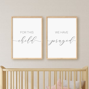 Può includere: Due stampe incorniciate con il testo "Per questo bambino abbiamo pregato" in un carattere di calligrafia moderna. Le stampe sono appese sopra una culla di legno con un cuscino a forma di stella rosa.