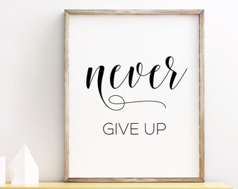 May include: A framed print with the text "never give up" in black cursive script on a white background. The frame is light brown wood and the print is sitting on a light brown wooden shelf with white shelves and white geometric shapes.