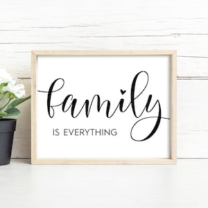 May include: A white framed print with black calligraphy that reads "family is everything" with a small heart symbol above the "i" in family.