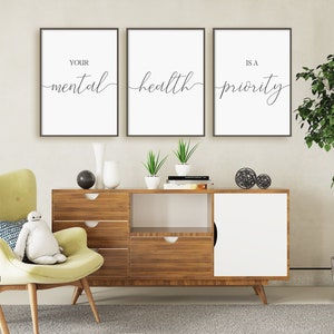 May include: Three framed prints with white backgrounds and black text. The text reads "Your mental health is a priority". The prints are hanging on a white wall above a wooden cabinet with a white door.