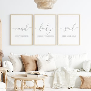 May include: Three framed wall art prints with the words "mind", "body", and "soul" in elegant script. Each print includes an inspirational phrase: "Open Your Mind", "Nourish Your Body", and "Feed Your Soul". The prints are displayed above a white sofa with decorative pillows.