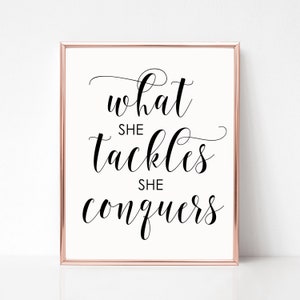 May include: A black and white printable wall art print with the text "what she tackles she conquers" in a cursive font.