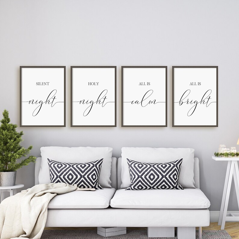 May include: Four framed art prints with the phrases "Silent Night," "Holy Night," "All is Calm," and "All is Bright" in elegant script. The prints are displayed above a white sofa with patterned pillows, creating a cozy, festive atmosphere.
