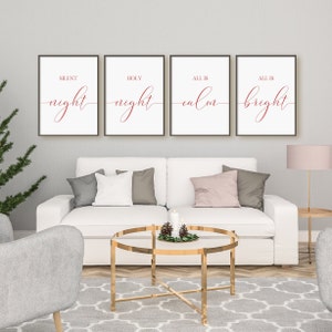 May include: Four framed art prints with the words "Silent Night", "Holy Night", "All is Calm", and "All is Bright" in red script on a white background. The prints are displayed above a white sofa with decorative pillows.