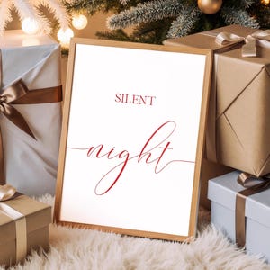 May include: A framed print with the words "SILENT night" in red script. The print is in a light wood frame and is surrounded by wrapped gifts and a Christmas tree. The gifts are wrapped in white, brown, and light blue paper with ribbons.