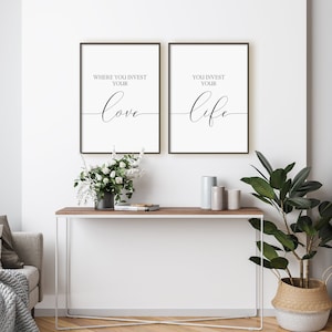 Pu&ograve; includere: Due stampe incorniciate nere con sfondi bianchi e testo nero. Il testo sulla stampa di sinistra recita "Where you invest your love" e il testo sulla stampa di destra recita "You invest your life". Le stampe sono appese a una parete bianca sopra un tavolo consolle in legno con una cornice in metallo bianco. Ci sono fiori bianchi in un vaso sul tavolo e una pianta in vaso con foglie verdi in un cesto intrecciato.