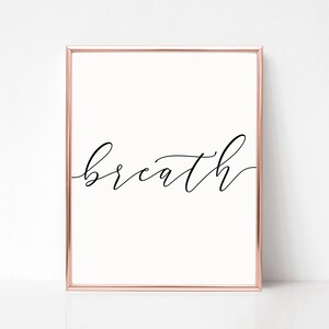 K&ouml;nnte beinhalten: Ein gerahmter Druck mit dem Wort "breath" in eleganter Schreibschrift. Der Rahmen ist in Ros&eacute;gold.