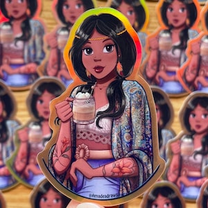 Puede incluir: Una pegatina holográfica dorada con una ilustración de dibujos animados de una mujer con el pelo largo y oscuro, vestida con una bata de patrones azules y blancos, sosteniendo un vaso de café helado. La pegatina tiene el texto "@Amadeadraws" en la parte inferior.
