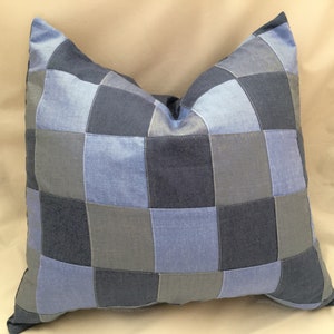 May include: A blue and gray patchwork pillow with a square pattern. The pillow is made of different shades of blue and gray fabric.