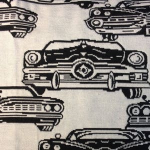 May include: A white fabric with a repeating pattern of black vintage cars. The cars are stylized with a pixelated design, giving them a retro aesthetic. The image is a close-up of the fabric, showcasing the detailed print.