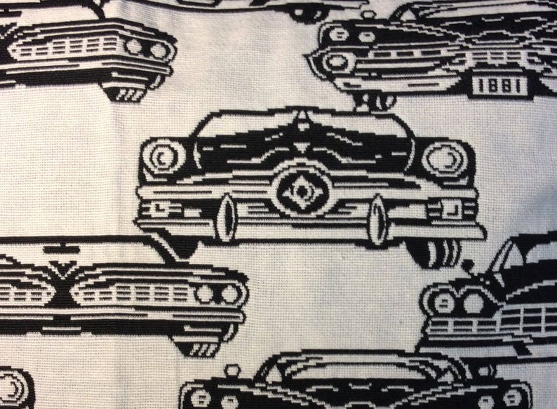 May include: A white fabric with a repeating pattern of black vintage cars. The cars are stylized with a pixelated design, giving them a retro aesthetic. The image is a close-up of the fabric, showcasing the detailed print.