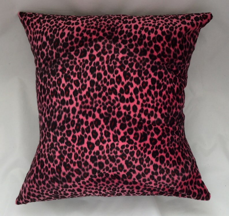 Puede incluir: Coj&iacute;n de decoraci&oacute;n de color rosa y negro con estampado de leopardo. El coj&iacute;n est&aacute; hecho de un tejido suave y afelpado.