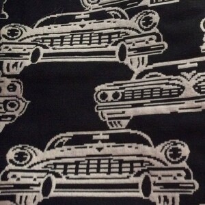 May include: Black and white fabric with a repeating pattern of vintage cars. The cars are stylized with a pixelated design, and some include the number "1881". The overall design is a retro aesthetic.