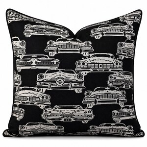 May include: A square throw pillow featuring a repeating pattern of white vintage cars on a solid black background. The design showcases various front-facing classic automobiles with detailed grilles, headlights, and bumpers, finished with black piping.