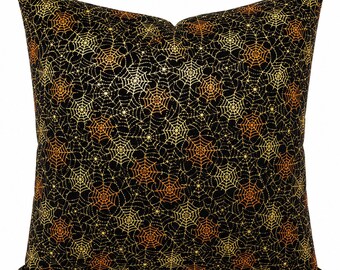 May include: A square throw pillow featuring a black background with a repeating pattern of spider webs in shades of gold, yellow, and orange. The web design is distributed evenly across the entire surface of the pillow, creating a dense, intricate, and continuous graphic print.