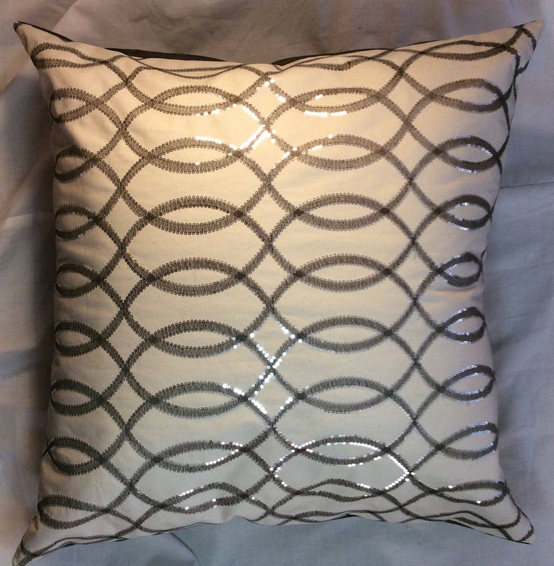 May include: A white throw pillow with a silver and black geometric pattern. The pattern is made up of interlocking ovals.