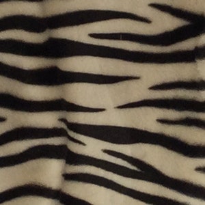 May include: Close-up of a fabric with a zebra stripe pattern. The stripes are black and the background is a light beige color. The fabric has a soft, textured appearance.