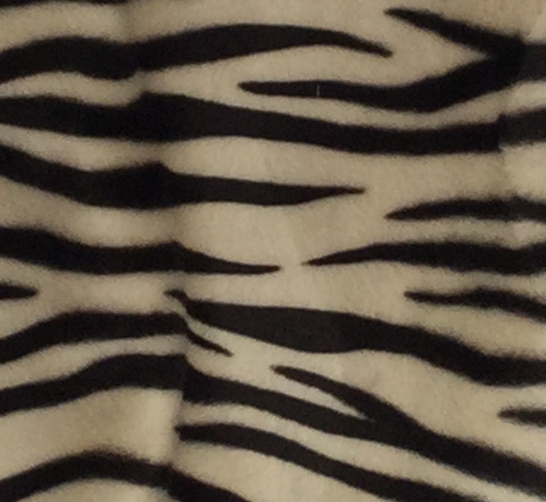 May include: Close-up of a fabric with a zebra stripe pattern. The stripes are black and the background is a light beige color. The fabric has a soft, textured appearance.