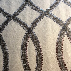 May include: Close-up of a white fabric with a silver and brown geometric pattern. The pattern is made of small sequins sewn in a repeating design of circles and diamonds.