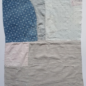 Peut inclure: Une pièce textile rectangulaire composée de divers morceaux de tissu cousus ensemble. Le patchwork présente des motifs floraux bleus, des rayures gris clair et blanches, et des sections rose pâle unies, assemblées par des coutures.