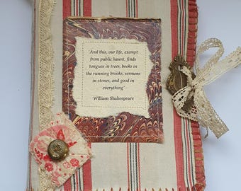 May include: Handmade journal with a red and white striped fabric cover. The journal features a decorative button, lace trim, and a quote from William Shakespeare. The quote is framed with marbled paper.