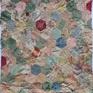 May include: A patchwork quilt top constructed from numerous hexagonal fabric pieces. The fabric patches feature a variety of colours including sage green, dusty pink, cream, deep red, and blue, with diverse floral and damask patterns.