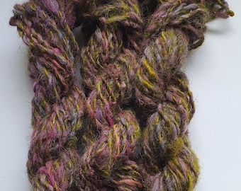 May include: A skein of yarn in shades of purple, green, and brown. The yarn is hand-spun and has a fuzzy texture.