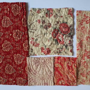 Pode incluir: Cinco amostras de tecido retangulares e quadradas com texturas acolchoadas. As peças exibem vários padrões, incluindo motivos florais vermelhos sobre fundo vermelho escuro, creme com rosas vermelhas, rosa claro sólido e creme com desenhos paisley.